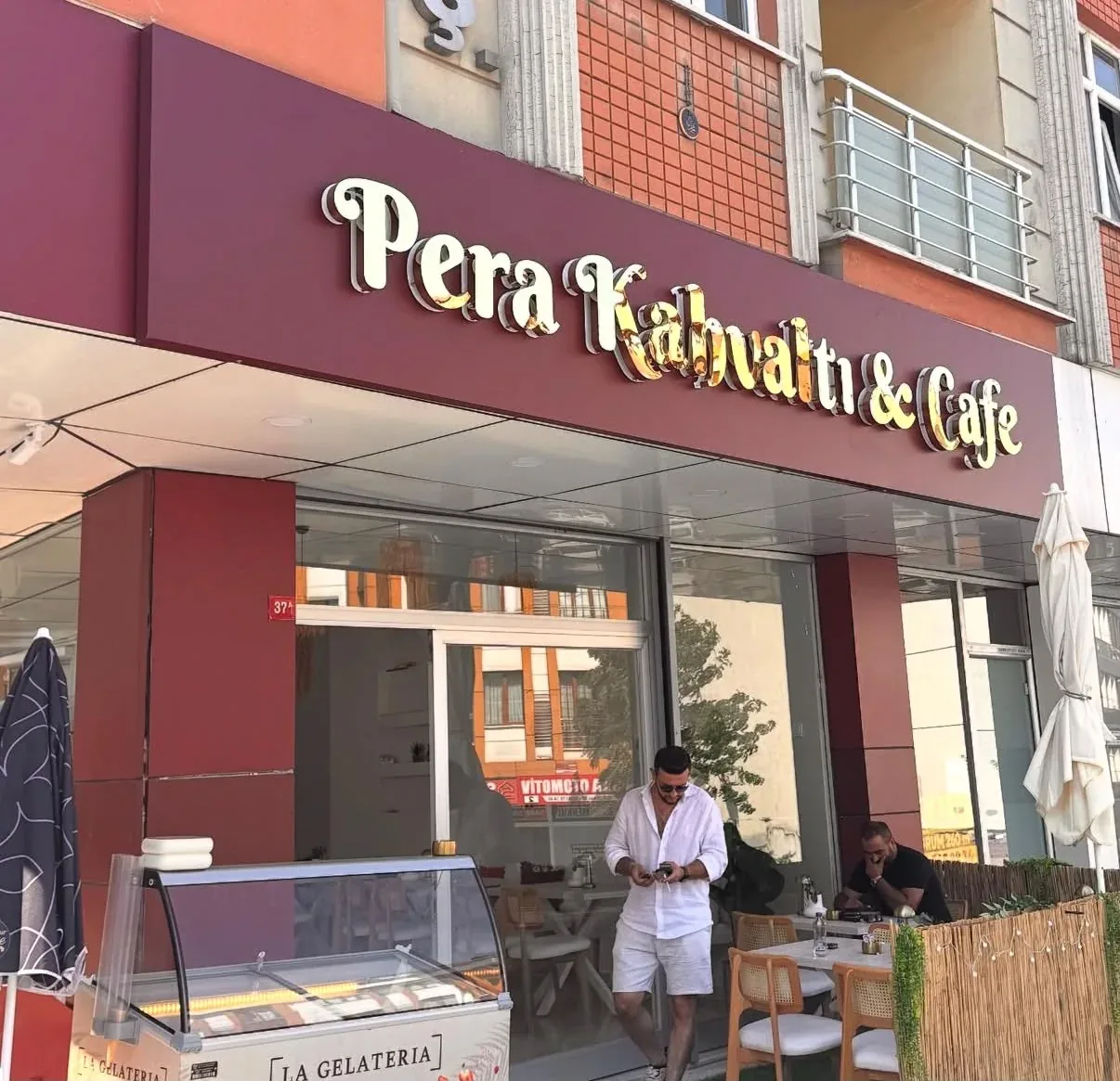 Koyu kahverengi dokulu duvar üzerinde sıcak turuncu halo ışıkla arkadan aydınlatılan siyah yüzeyli kutu harfler ve logo bloğu — Dekupe alt satır yakın plan