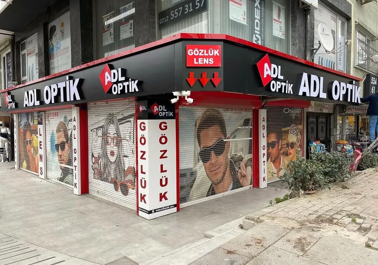 Akşam saatinde kafe vitrin camında delikli folyo üzerine basılmış büyük kahve fincanı görseli, önünde ahşap masa ve metal sandalyeler — Doğrama hizası görünümü